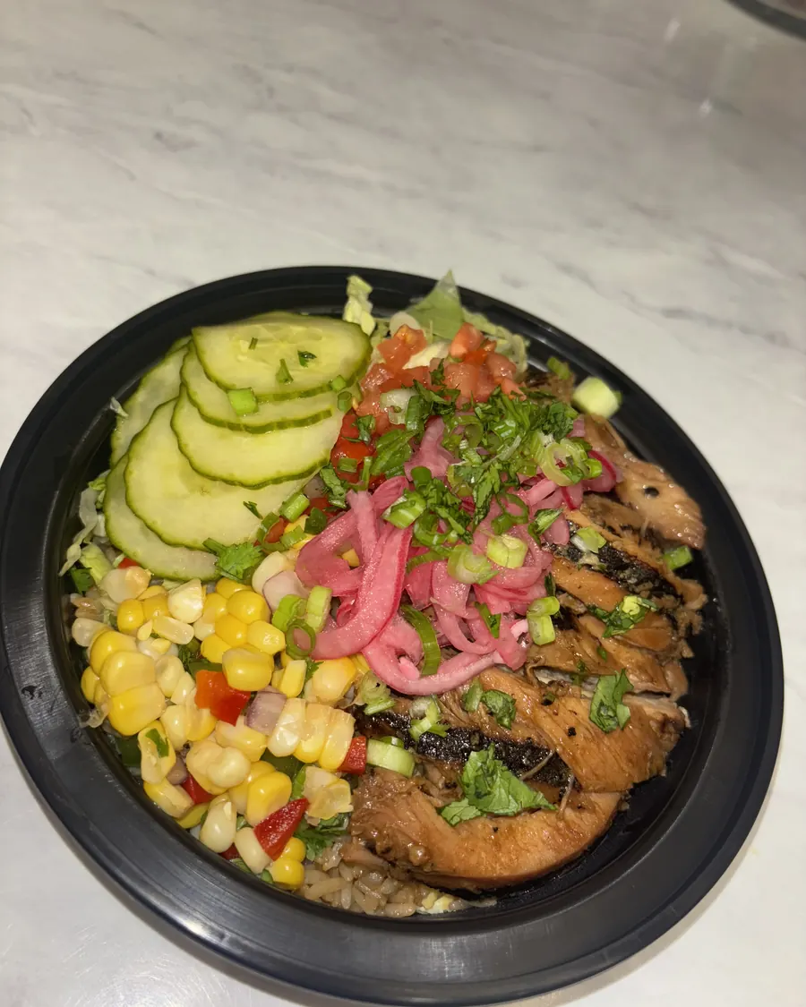 Bourbon chicken bowl topped with pickled red onion, corn, cucumber and fresh herbs